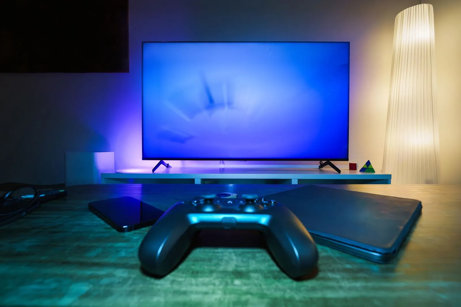 Televisor con retroiluminación LED azul y morada detrás y un mando de consola delante
