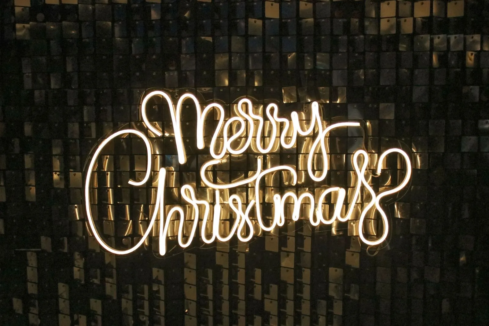 Cartel neón LED cálido con la frase Merry Christmas sobre una pared de lentejuelas