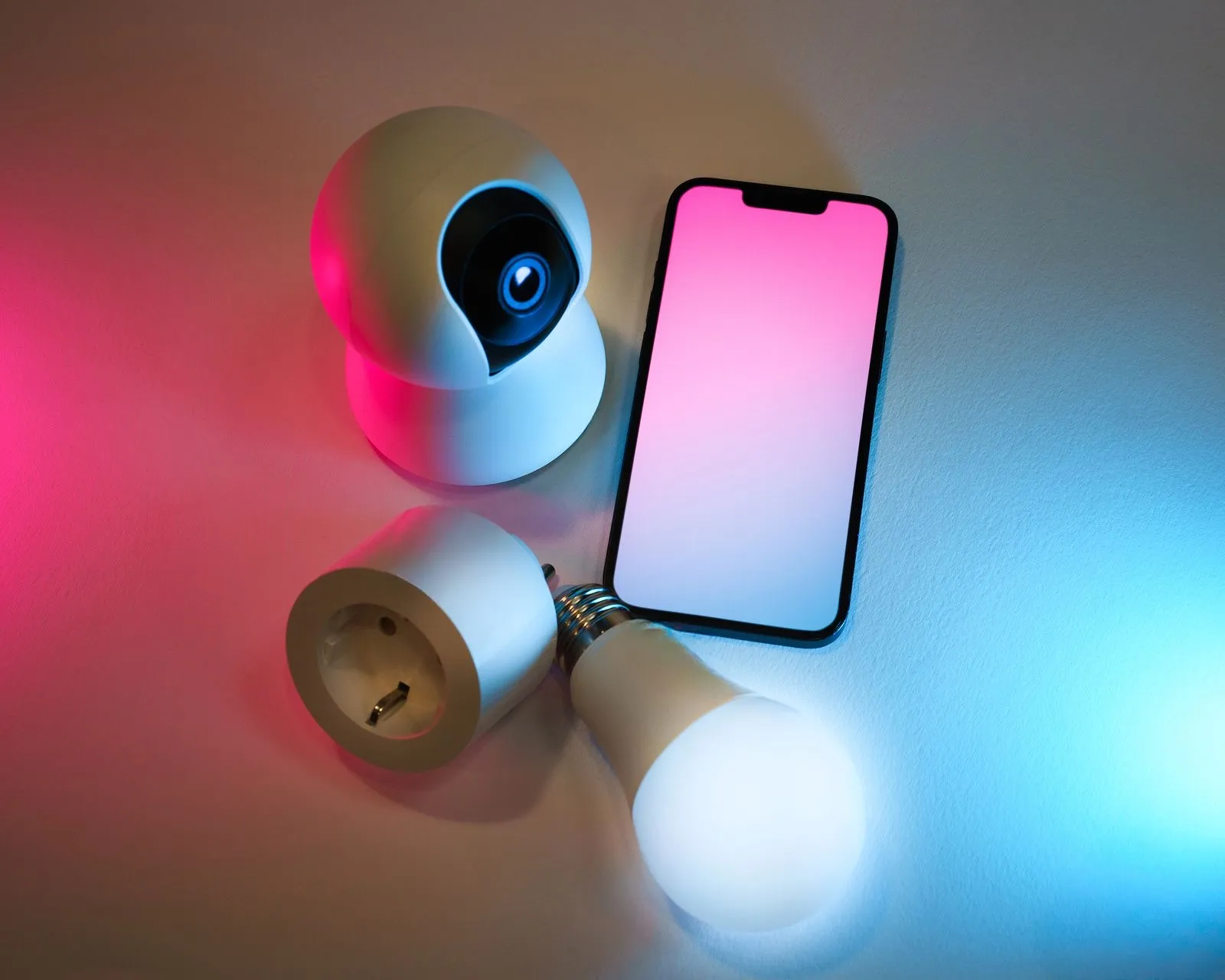 Bombilla inteligente, enchufe, cámara y móvil iluminados con luz rosa y azul