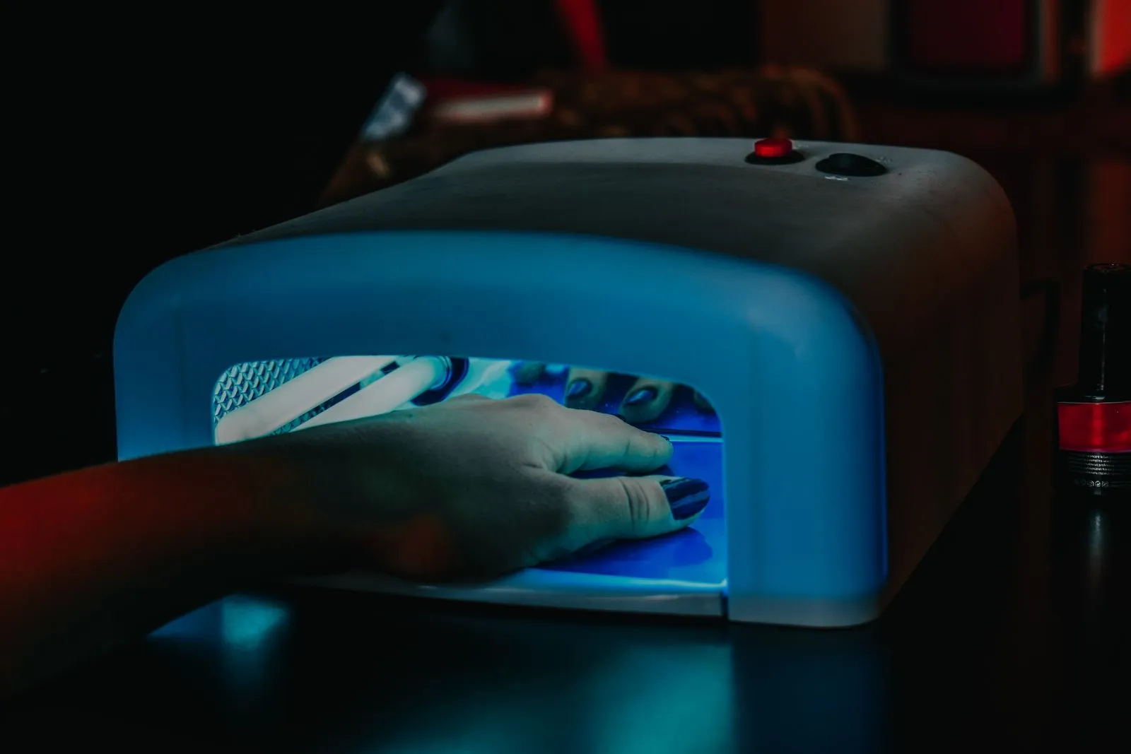 Mano dentro de una lámpara ultravioleta de uñas encendida con luz azul