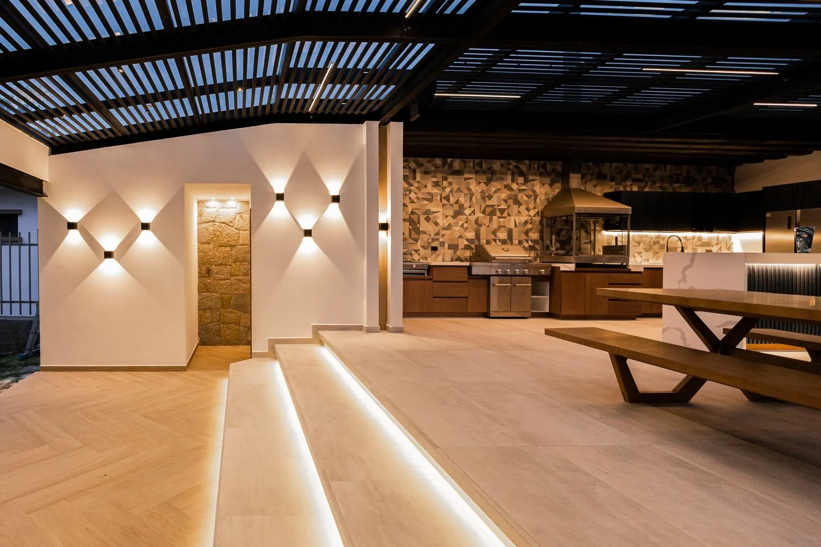 Patio exterior con tiras LED cálidas bajo los escalones y apliques en la pared