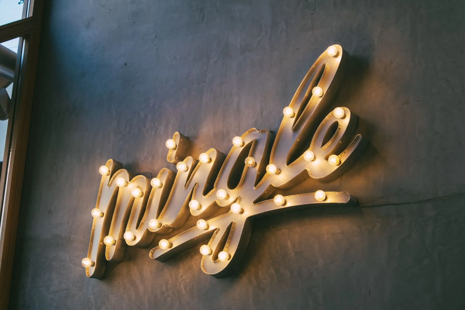 Palabra en letras luminosas con bombillas cálidas colgada en una pared gris