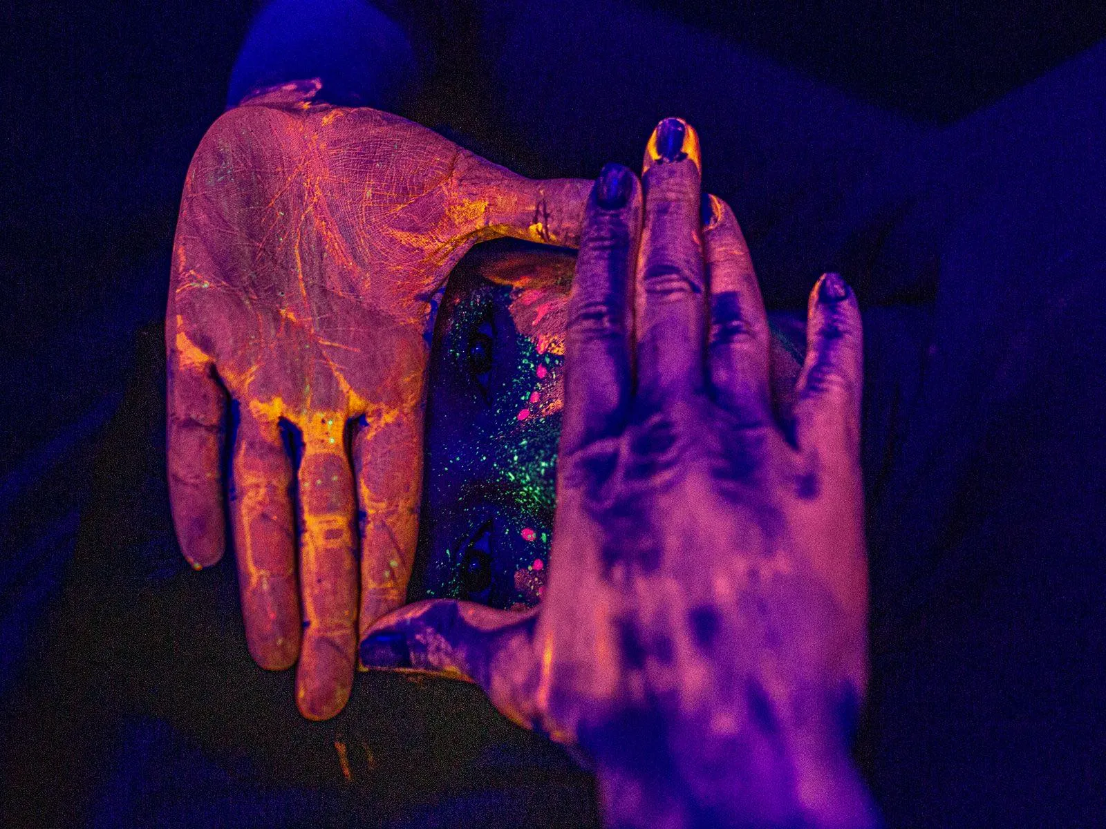 Manos con pintura fluorescente naranja y morada iluminadas con luz negra UV