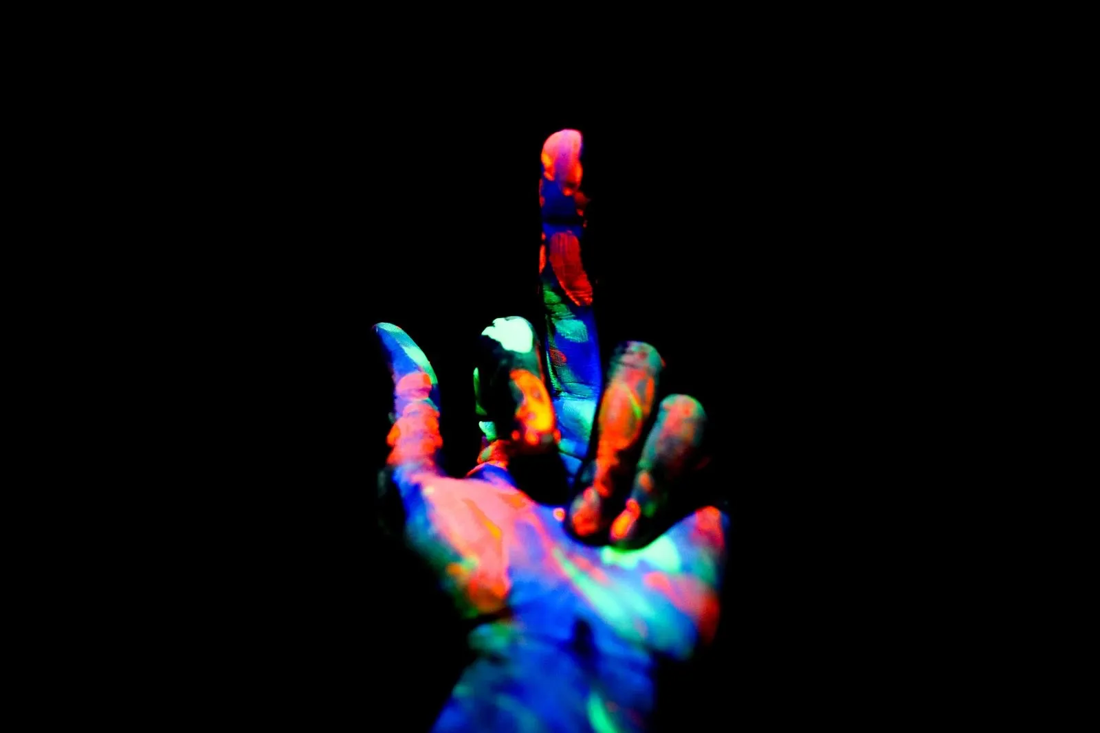 Mano con pintura fluorescente que reacciona a un foco de luz negra en la oscuridad