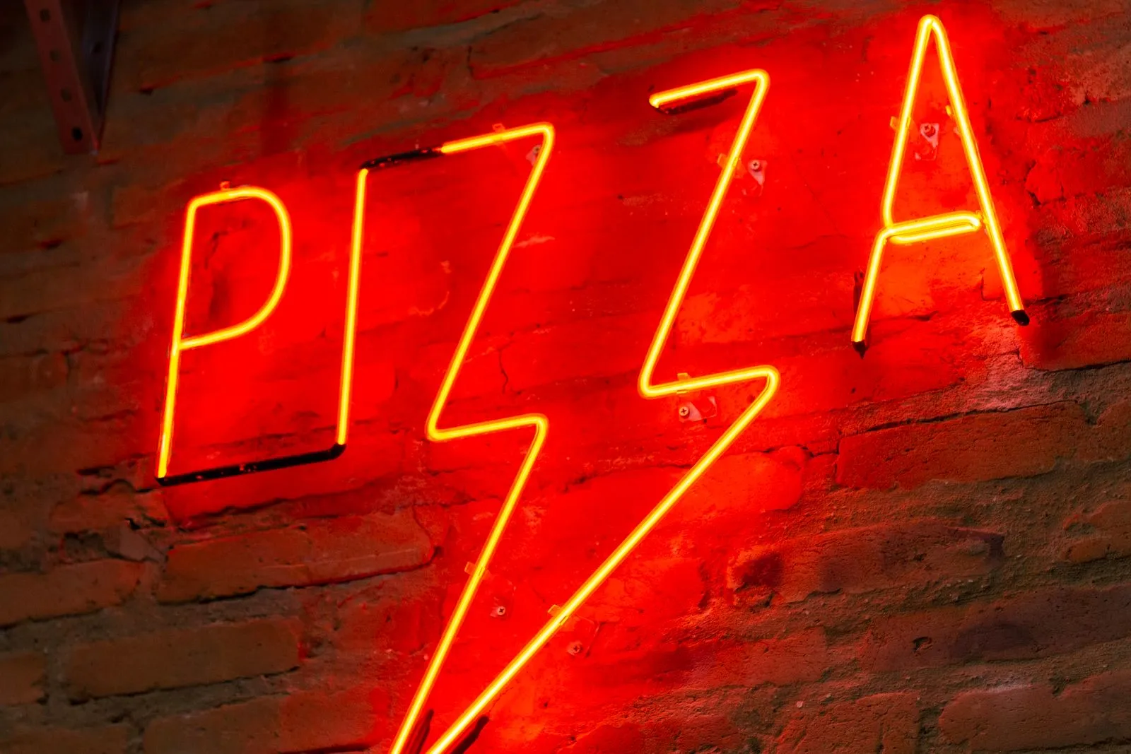 Cartel neón LED rojo con la palabra pizza y un rayo sobre ladrillo