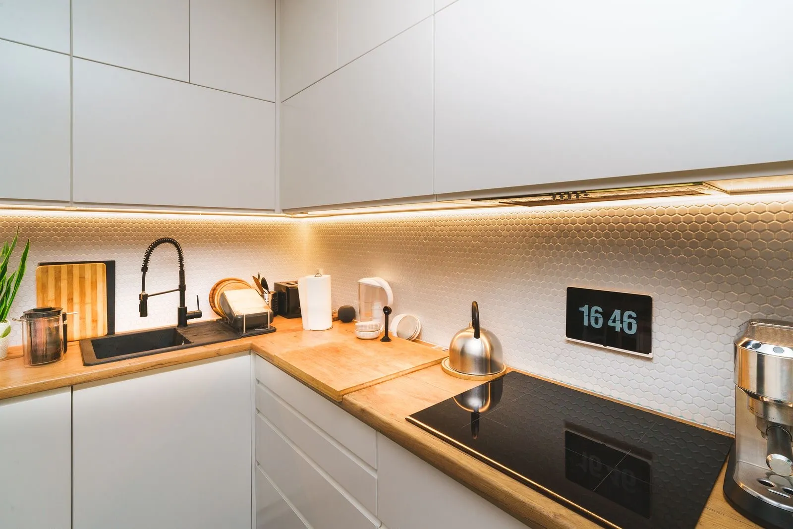 Cocina blanca con tira LED cálida bajo los muebles altos iluminando la encimera de madera
